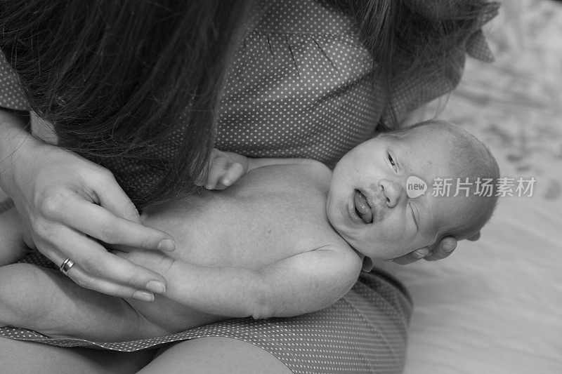 Mom's hands are holding the baby carefully. A serious and beautiful newborn baby is sleeping. The concept of maternal tenderness.